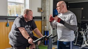Man on a fitness bike talking with the Personal Trainer looking after him and discussing gym memberships and other gyms in Huddersfield